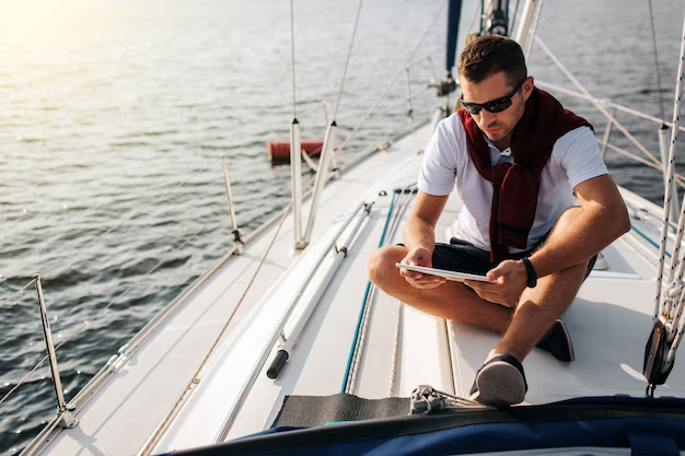 A man with glasses sits on the deck and holds a tablet in his hands