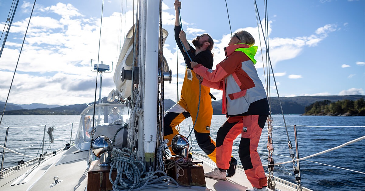 Two men in uniform tighten a sail