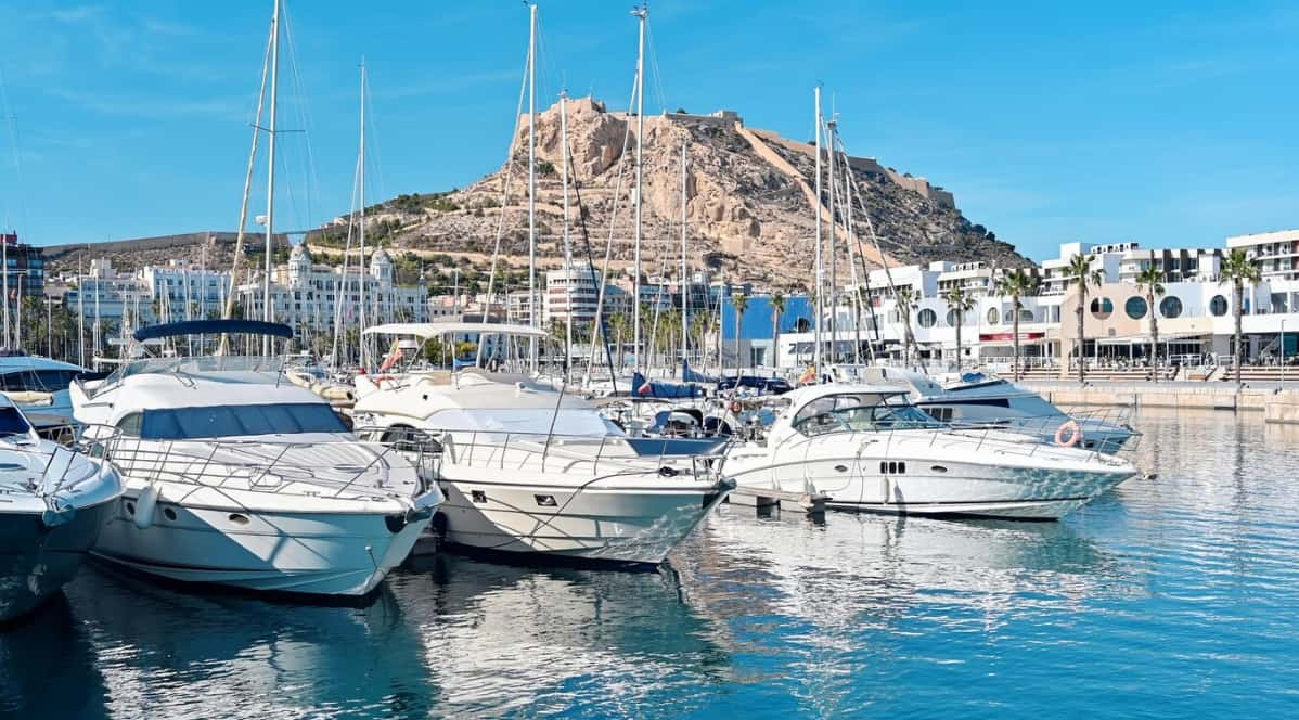 Yachts and sailboats docked in a sunny marina with a hilltop fort