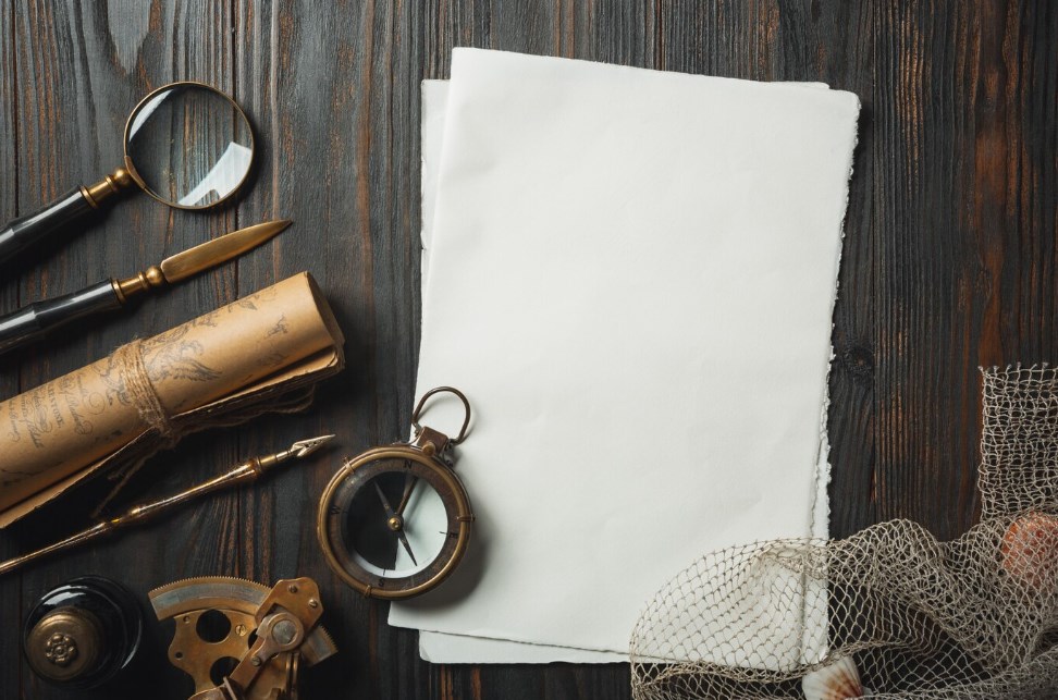 sail logging concept: old-fashioned compass, a roll of old paper, blank paper sheets, writing accessories, and a fishing net on a dark wooden table