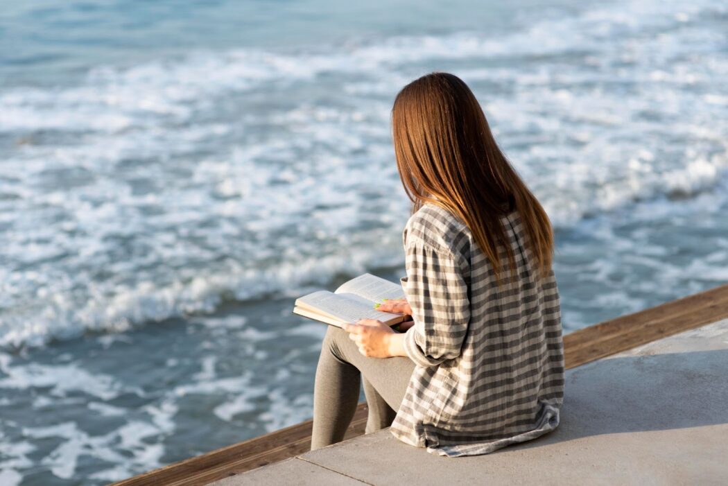 Back view of woman reading next to the sea